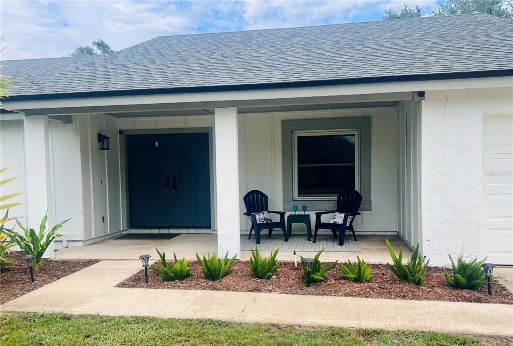 A front porch with two chairs, a dark blue double door, and a landscaped garden — 7432 SPARKLING LAKE RD, ORLANDO, FL