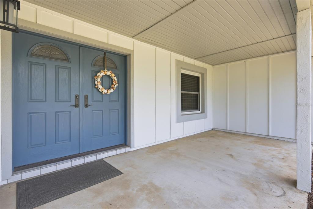 A covered concrete porch features blue double front doors with a wreath and a window — 7432 SPARKLING LAKE RD, ORLANDO, FL