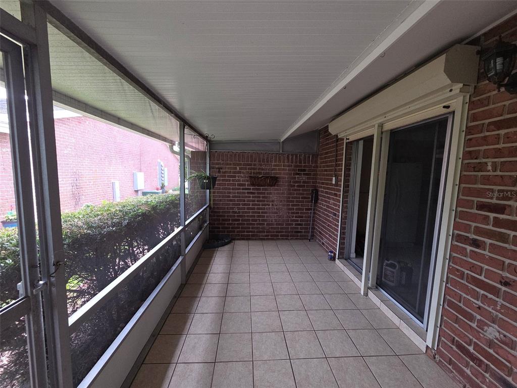 A screened-in porch with tiled flooring, brick walls, and a sliding glass door — 5860 LA COSTA DRIVE, ORLANDO, FL