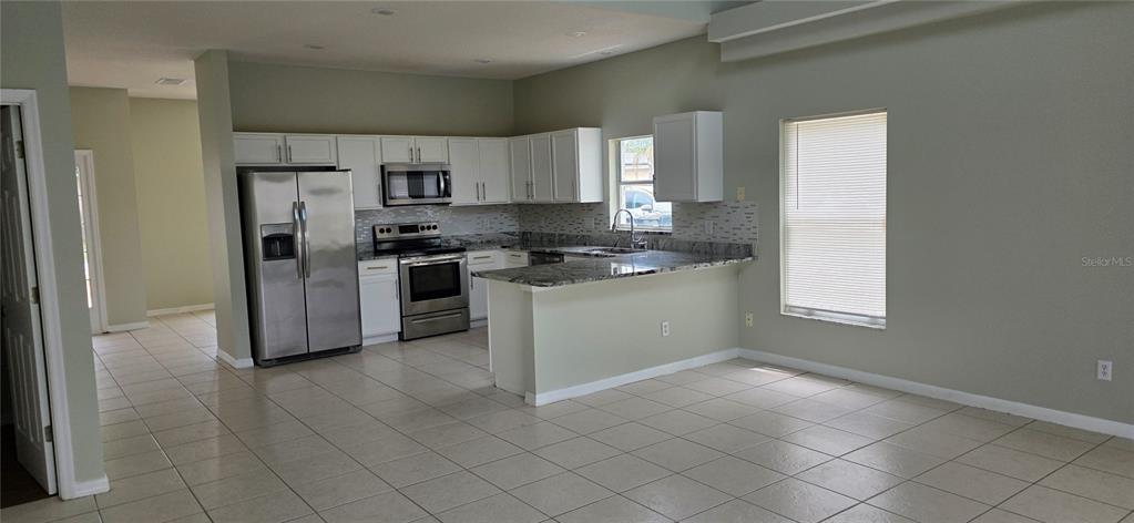 A kitchen with white cabinets, stainless steel appliances, granite countertops, and light tile flooring — 103 RIGGS CIRCLE, DAVENPORT, FL