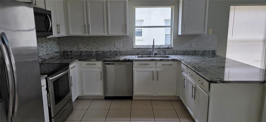 A kitchen features white cabinets, granite countertops, stainless steel appliances, and a tile backsplash — 103 RIGGS CIRCLE, DAVENPORT, FL