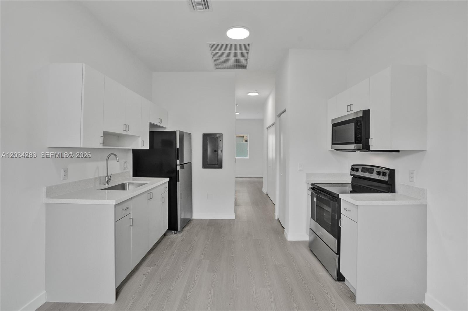 A modern galley kitchen features white cabinets, stainless steel appliances, and light wood-look flooring — 1567 NW 1st St # 3, Miami FL 33125, MIAMI, FL