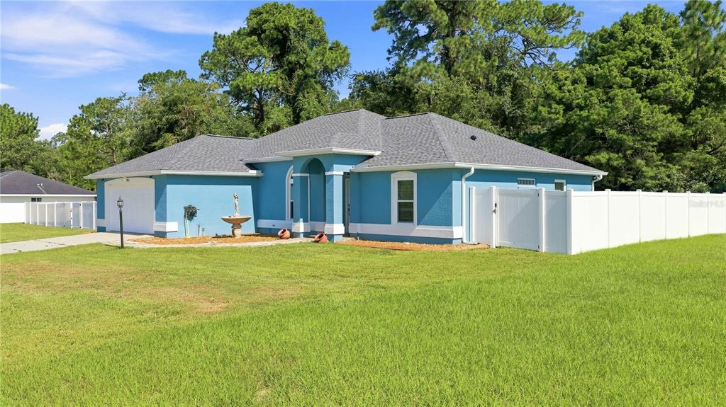 A blue single-story house with a white fence, a gray roof, and a front fountain — 7411 SW 128TH STREET, OCALA, FL