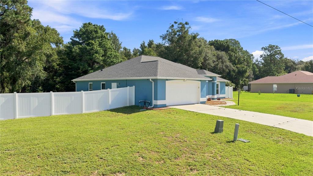 A blue single-story house with a white garage door and a white vinyl fence — 7411 SW 128TH STREET, OCALA, FL