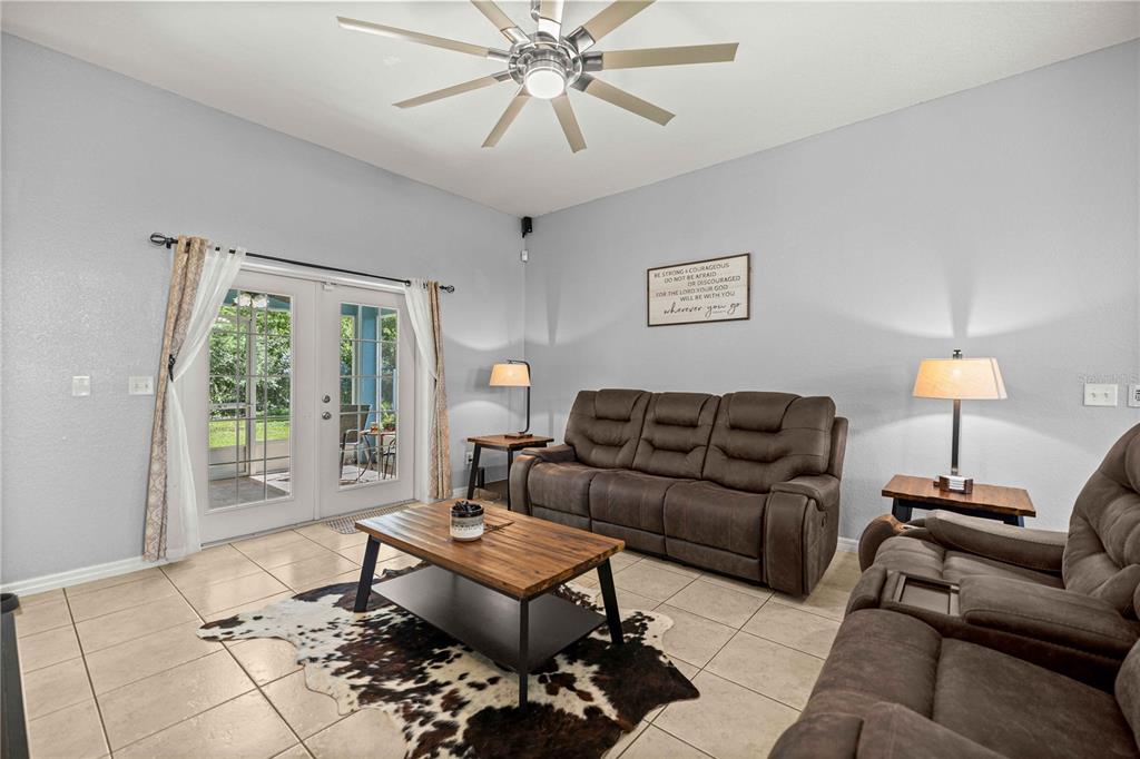 A living room features tile floors, brown reclining sofas, a coffee table, and glass patio doors — 7411 SW 128TH STREET, OCALA, FL