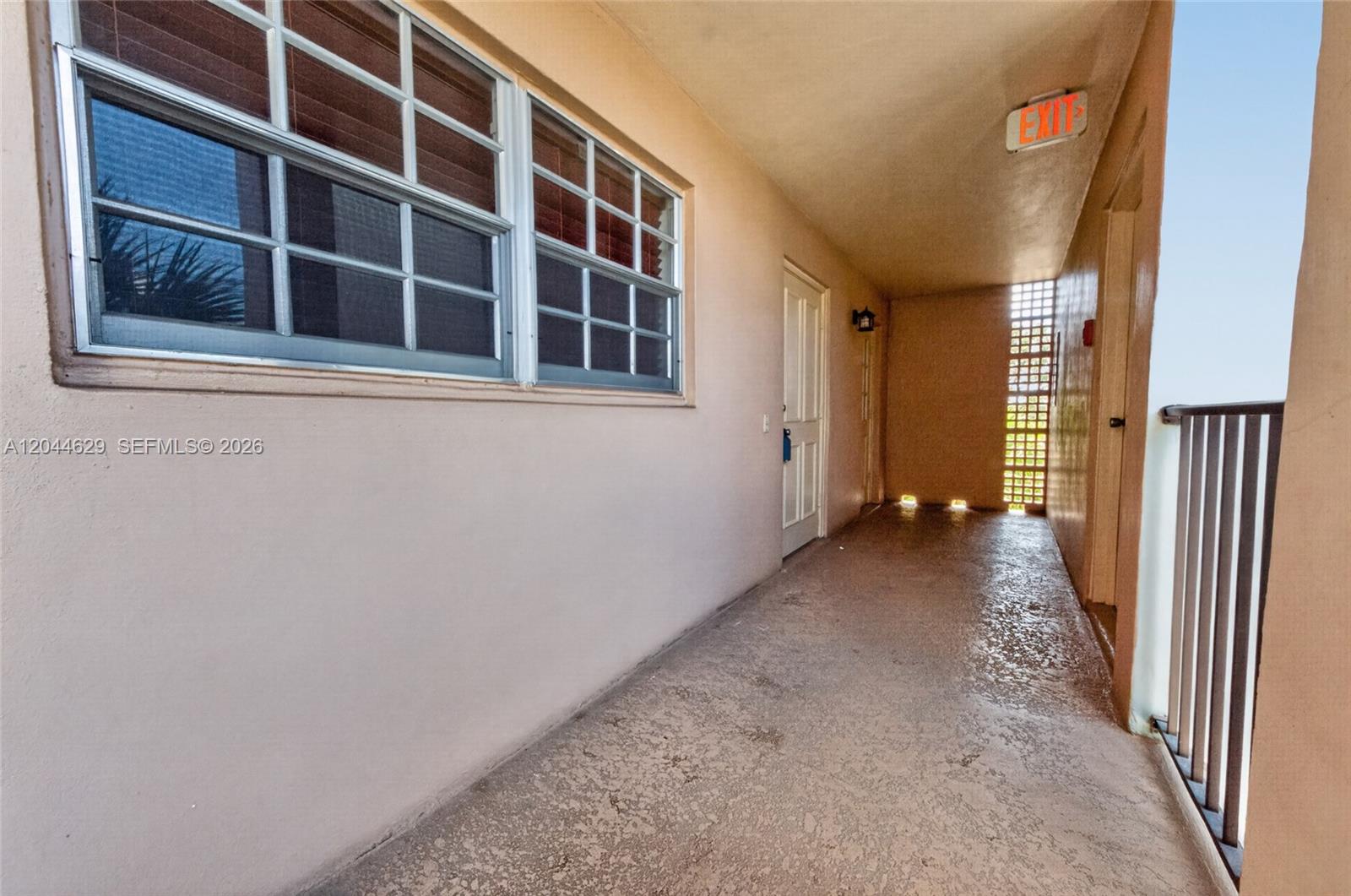 An outdoor apartment building walkway features a beige wall, a window, and a metal railing — 9101 W Sample Rd # 306, Coral Springs FL 33065, CORAL SPRINGS, FL
