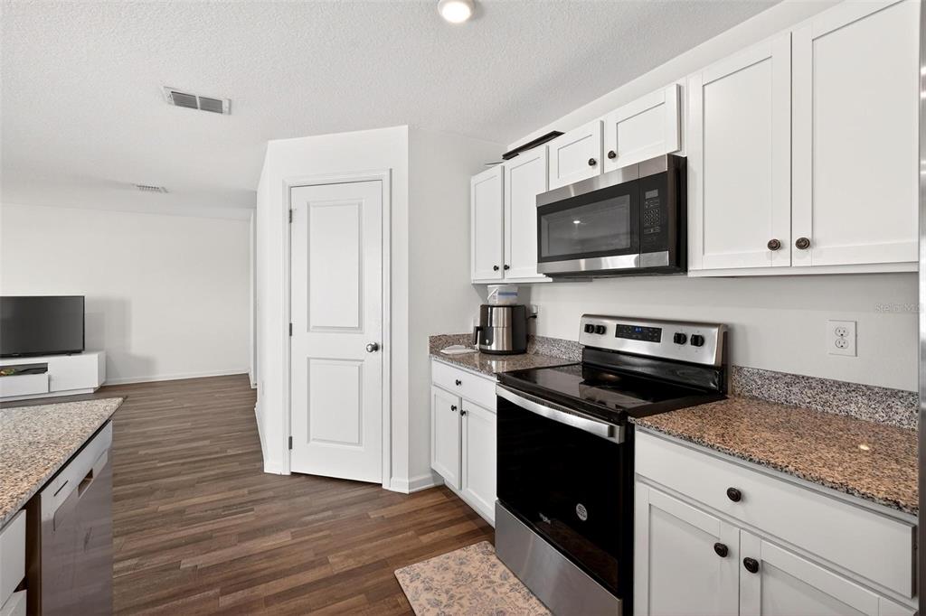A kitchen with white cabinets, granite countertops, stainless steel appliances, and wood-look flooring — 1665 MINNESOTA ROAD, SUMTERVILLE, FL