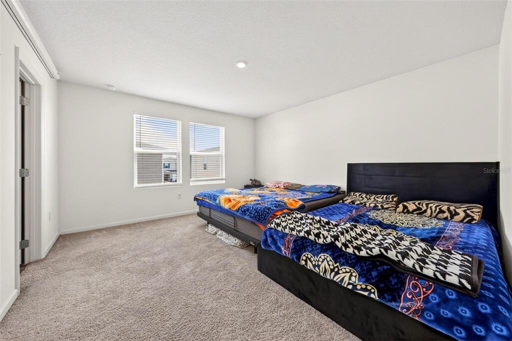 A bedroom features beige carpeting, white walls, two windows, and two beds with patterned blankets — 1665 MINNESOTA ROAD, SUMTERVILLE, FL