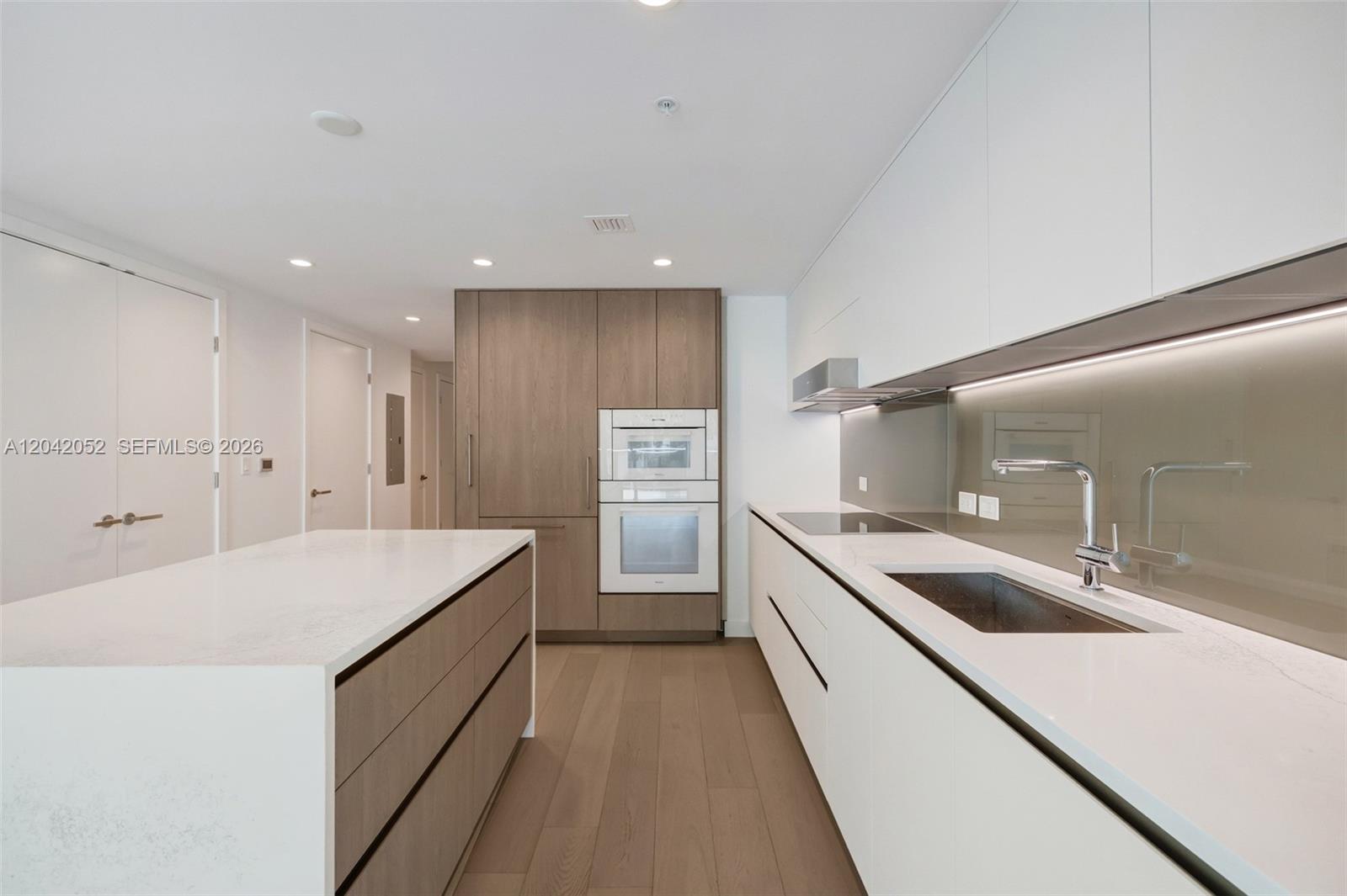 A modern kitchen features white countertops, wood-toned cabinetry, and stainless steel appliances — 9221 E Bay Harbor Drive # 210, Surfside FL 33154, SURFSIDE, FL