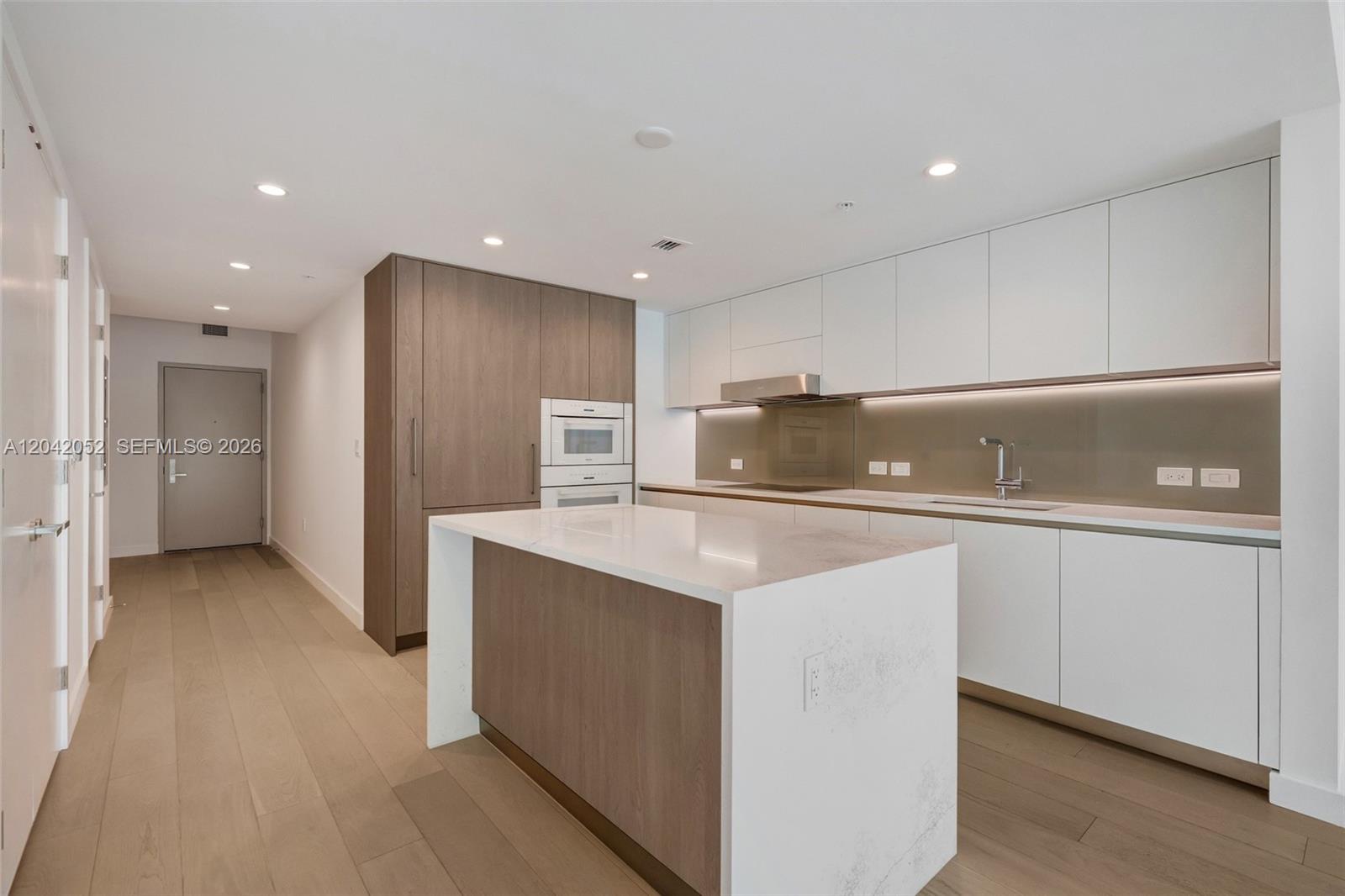 A modern kitchen features white cabinetry, a wood-paneled island, and light wood flooring — 9221 E Bay Harbor Drive # 210, Surfside FL 33154, SURFSIDE, FL