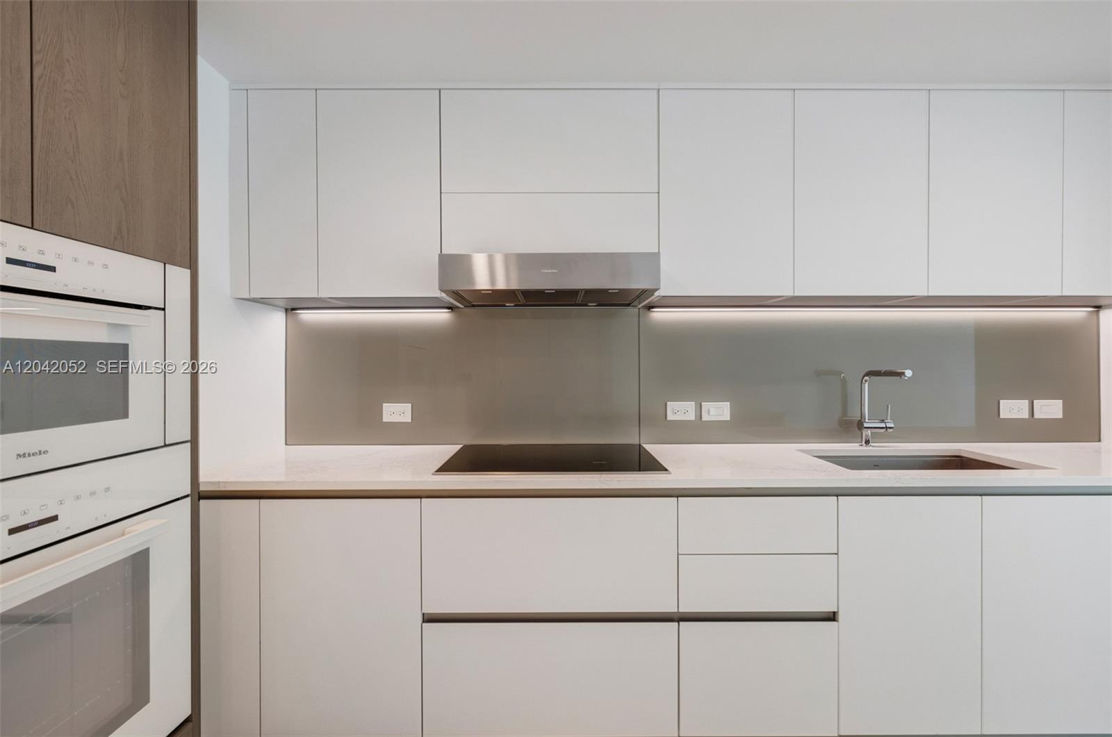 A modern kitchen features white cabinetry, a stainless steel range hood, and a glass backsplash — 9221 E Bay Harbor Drive # 210, Surfside FL 33154, SURFSIDE, FL