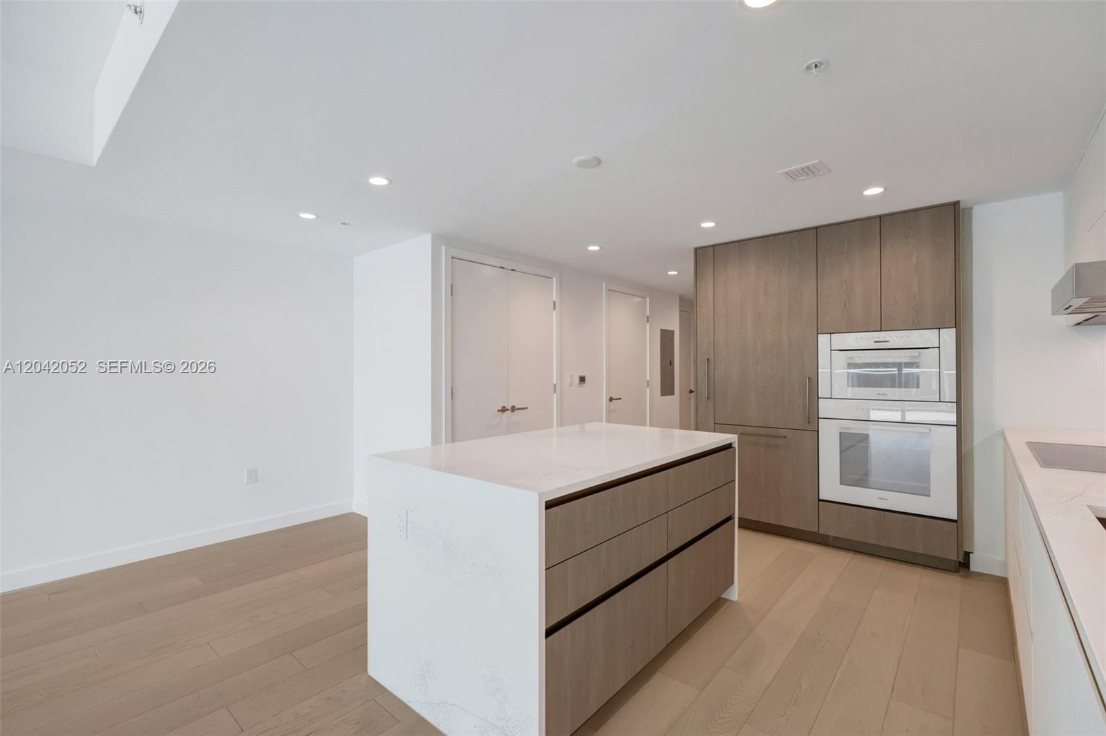 A modern kitchen features light wood flooring, white countertops, and wood-toned cabinetry — 9221 E Bay Harbor Drive # 210, Surfside FL 33154, SURFSIDE, FL