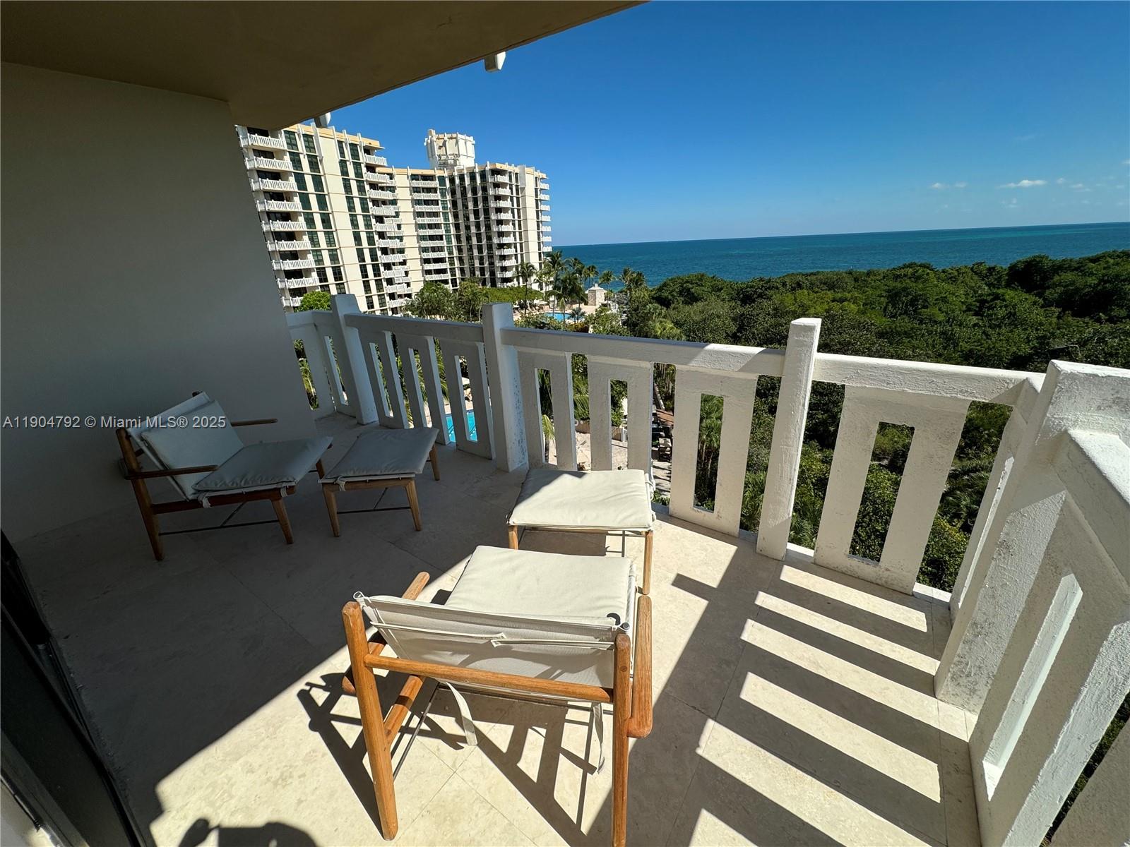 A balcony with outdoor furniture overlooks a lush landscape and the ocean — 1121 Crandon Blvd # D608, Key Biscayne FL 33149, KEY BISCAYNE, FL