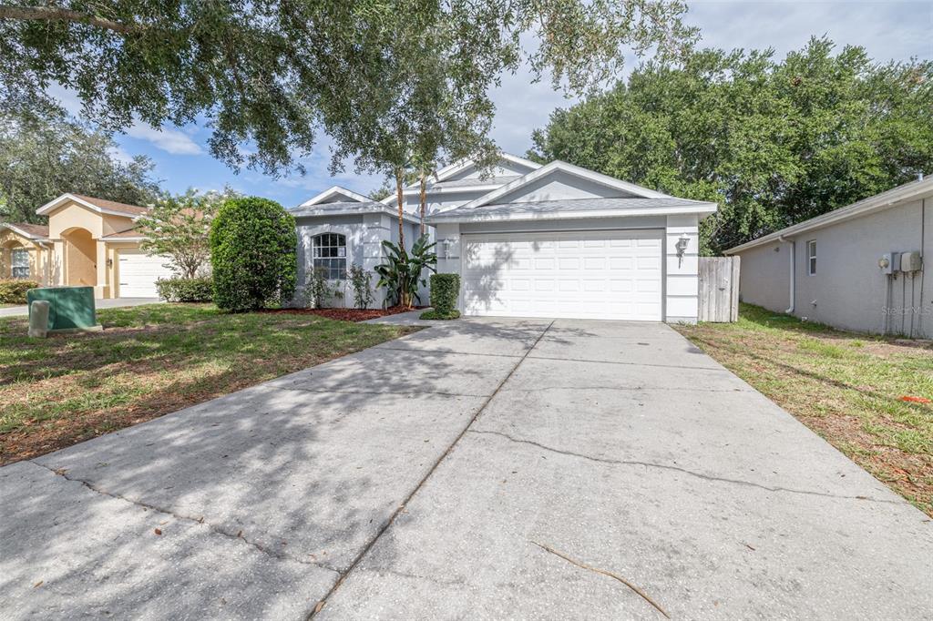 A single-story house with a white garage door, concrete driveway, and surrounding trees — 7805 BRISBANE COURT, NEW PORT RICHEY, FL