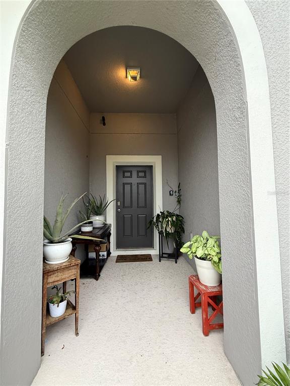 An arched entryway leads to a dark front door flanked by potted plants on stands — 12245 PRAIRIE PLANTATION WAY, ORLANDO, FL