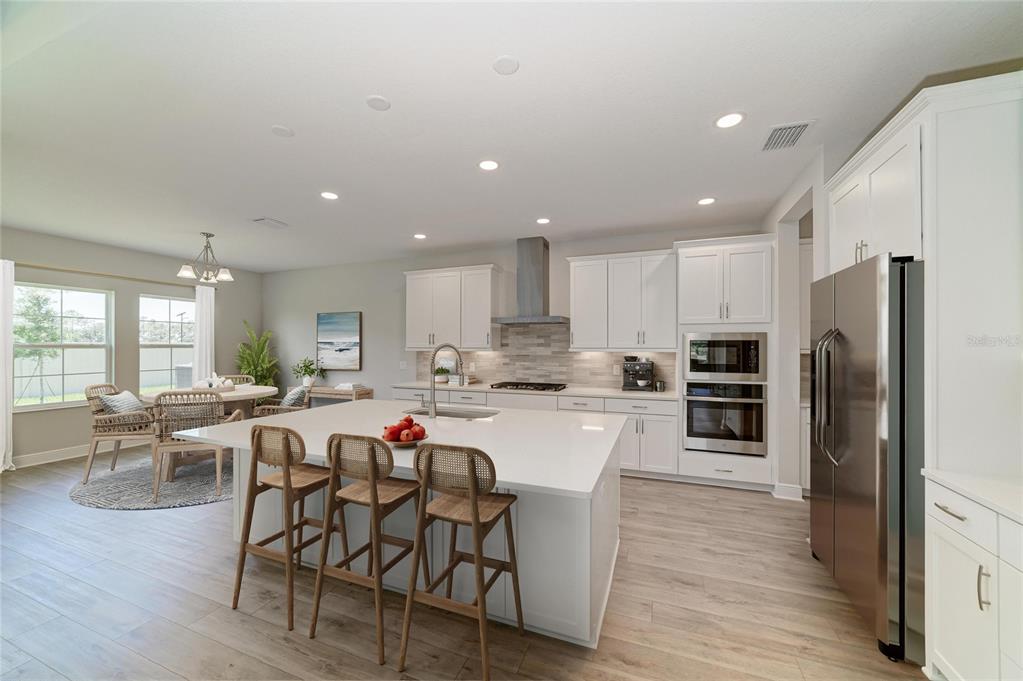 A modern kitchen features white cabinetry, a large quartz island with barstools, and wood-look flooring — 33496 TWILIGHT SEA PLACE, DADE CITY, FL