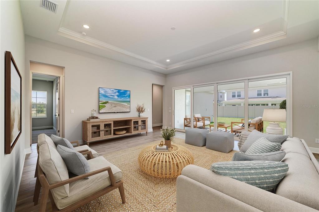 A living room features a tray ceiling, wood-look flooring, a media console, and sliding glass doors — 33496 TWILIGHT SEA PLACE, DADE CITY, FL