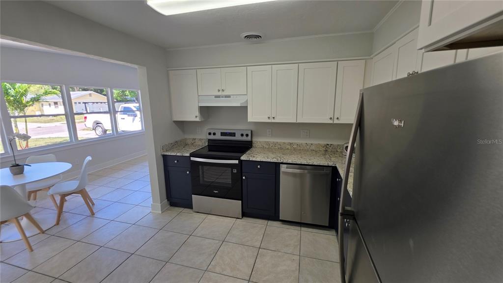 A kitchen features white upper cabinets, dark lower cabinets, stainless steel appliances, and tile flooring — 3167 IRVING STREET, SARASOTA, FL
