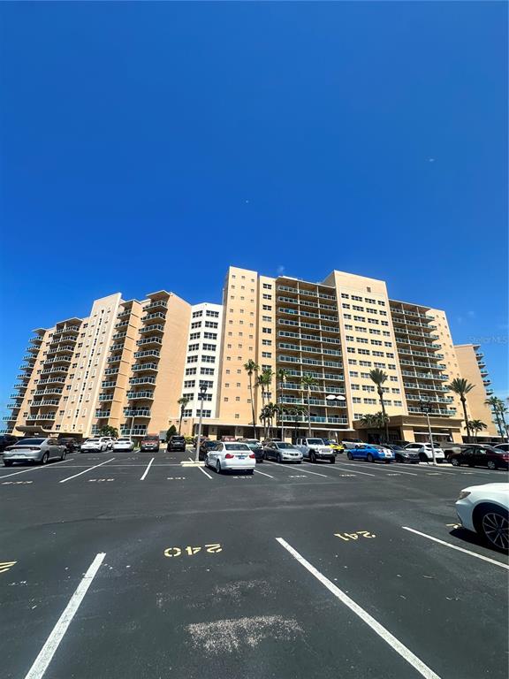 A large, multi-story tan apartment building stands behind a paved parking lot — 880 MANDALAY AVENUE UNIT 309, CLEARWATER, FL