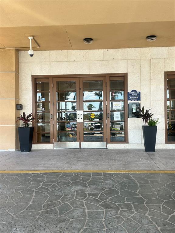 The entrance to a building features glass double doors flanked by two potted plants — 880 MANDALAY AVENUE UNIT 309, CLEARWATER, FL