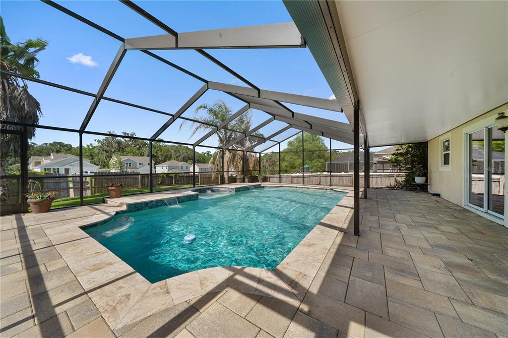 A screened-in patio features a rectangular swimming pool with water features and stone pavers — 14308 NW 161ST AVENUE, ALACHUA, FL
