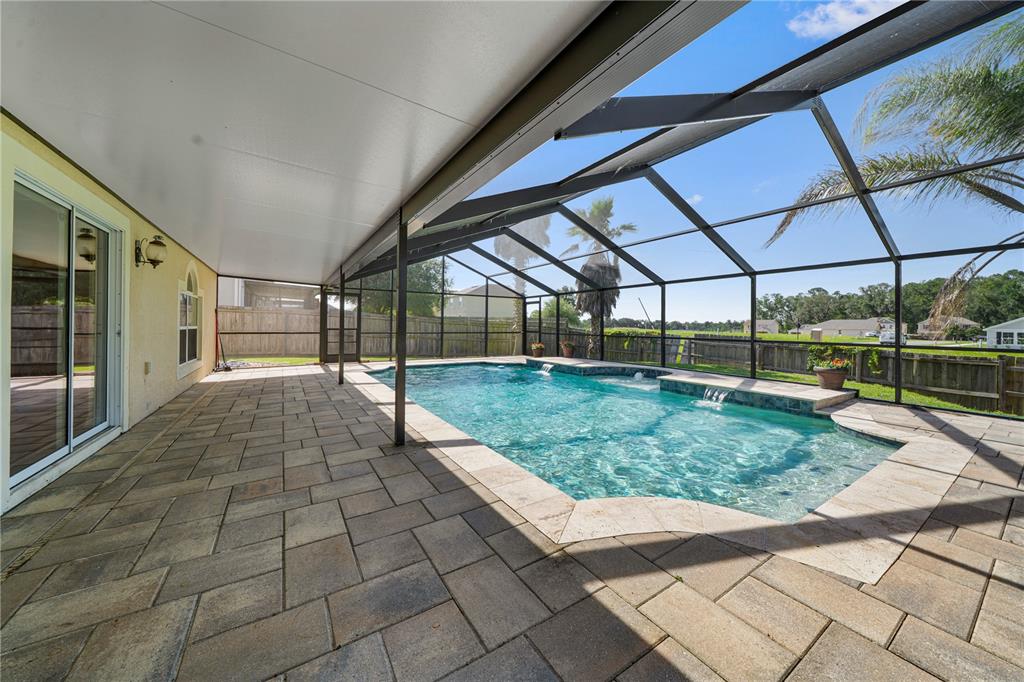 A covered patio with stone pavers overlooks a swimming pool enclosed by a screen cage — 14308 NW 161ST AVENUE, ALACHUA, FL