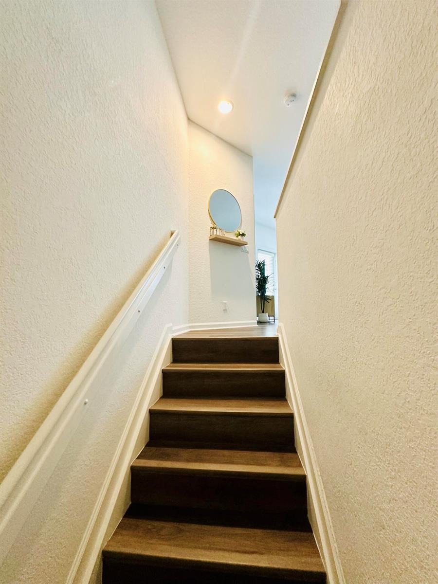A staircase with dark wood treads leads to a landing featuring a small wall mirror — 4802 W Bexley Park Drive # A, Delray Beach FL 33445, DELRAY BEACH, FL