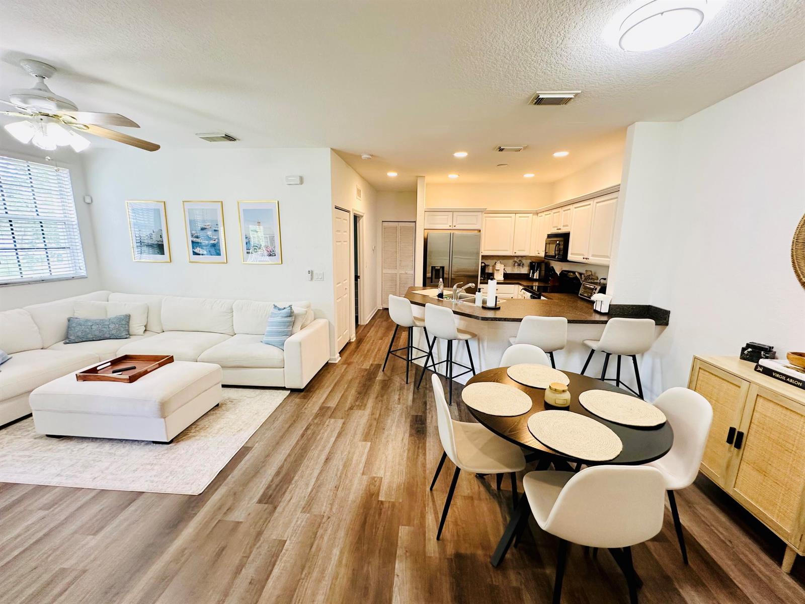 An open-concept living and dining area features white furniture, wood-look flooring, and a kitchen island — 4802 W Bexley Park Drive # A, Delray Beach FL 33445, DELRAY BEACH, FL