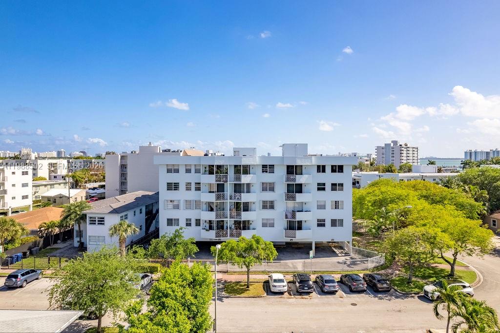 An exterior view of a multi-story white apartment building with a ground-level parking area — 1990 Marseille Dr # 402, Miami Beach FL 33141, MIAMI BEACH, FL