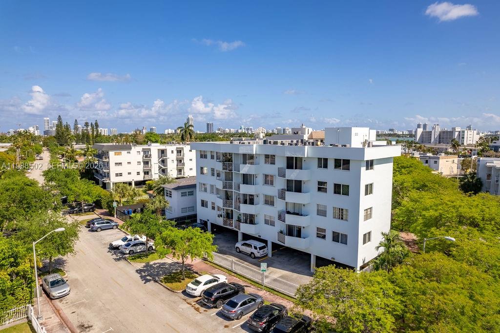 An aerial view shows a multi-story white apartment building with a ground-level parking area — 1990 Marseille Dr # 402, Miami Beach FL 33141, MIAMI BEACH, FL