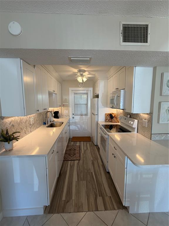 A galley kitchen features white cabinets, quartz countertops, a herringbone backsplash, and wood-look flooring — 3808 GULF OF MEXICO DRIVE UNIT E105, LONGBOAT KEY, FL