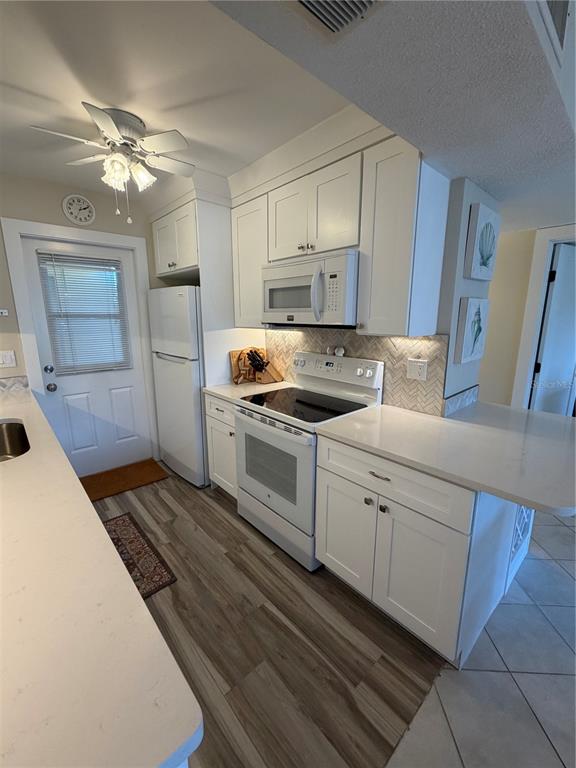 A kitchen features white cabinets, stainless steel appliances, a herringbone backsplash, and wood-look flooring — 3808 GULF OF MEXICO DRIVE UNIT E105, LONGBOAT KEY, FL