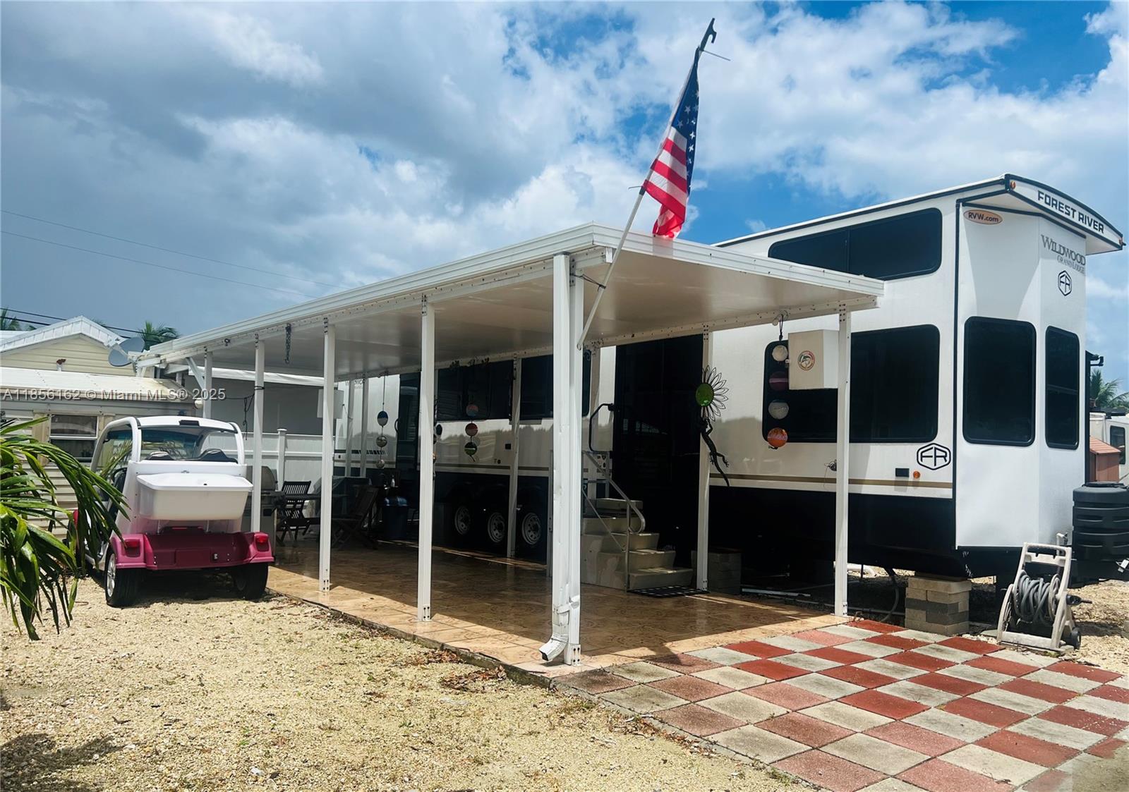 A Forest River Wildwood RV sits under a metal carport next to a small golf cart — 325 Calusa St Lot 301, Key Largo FL 33037, KEY LARGO, FL