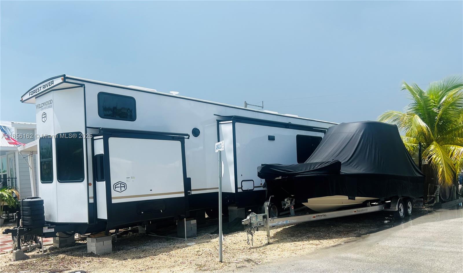 A white Forest River Wildwood Grand Lodge travel trailer is parked next to a covered boat — 325 Calusa St Lot 301, Key Largo FL 33037, KEY LARGO, FL