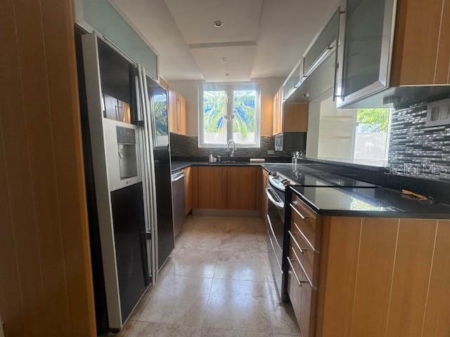 A kitchen features wood cabinets, black countertops, stainless steel appliances, and light-colored tile flooring — 1124 MANSIONES DE VISTAMAR MARINA III, CAROLINA, PR
