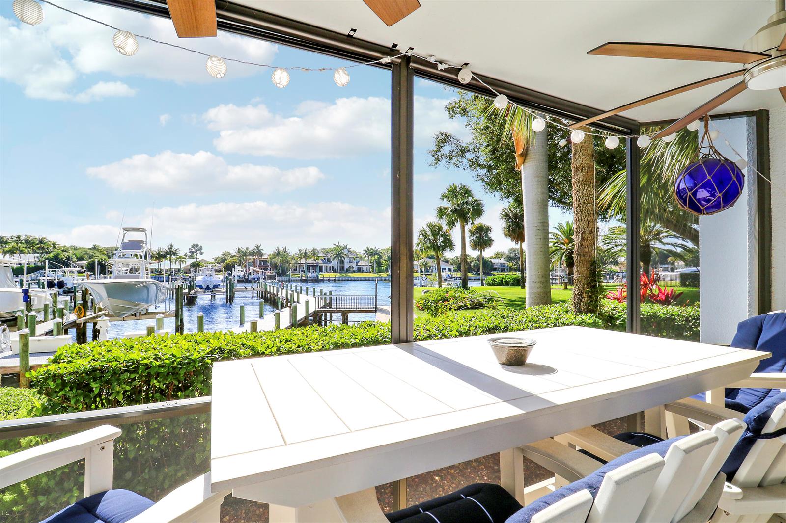 A screened-in patio features a white dining table overlooking a canal with docked boats — 515 Bay Colony Drive N, Juno Beach FL 33408, JUNO BEACH, FL