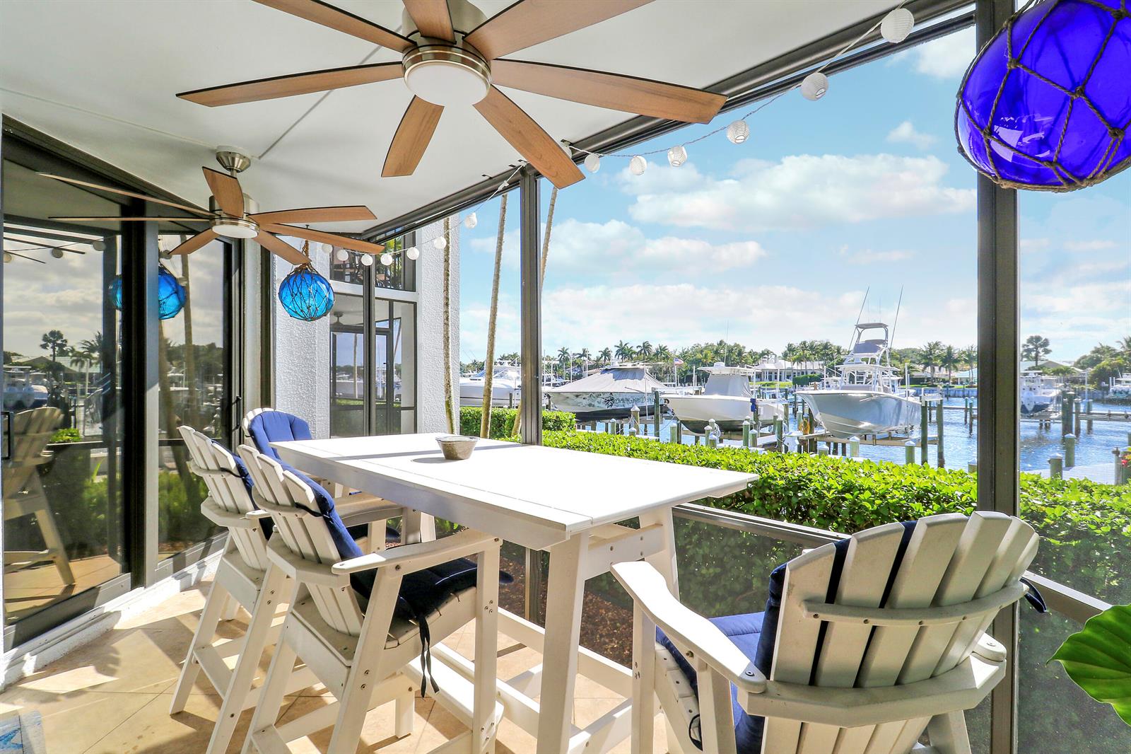 A screened-in patio features a dining set, ceiling fans, and a view of a marina — 515 Bay Colony Drive N, Juno Beach FL 33408, JUNO BEACH, FL