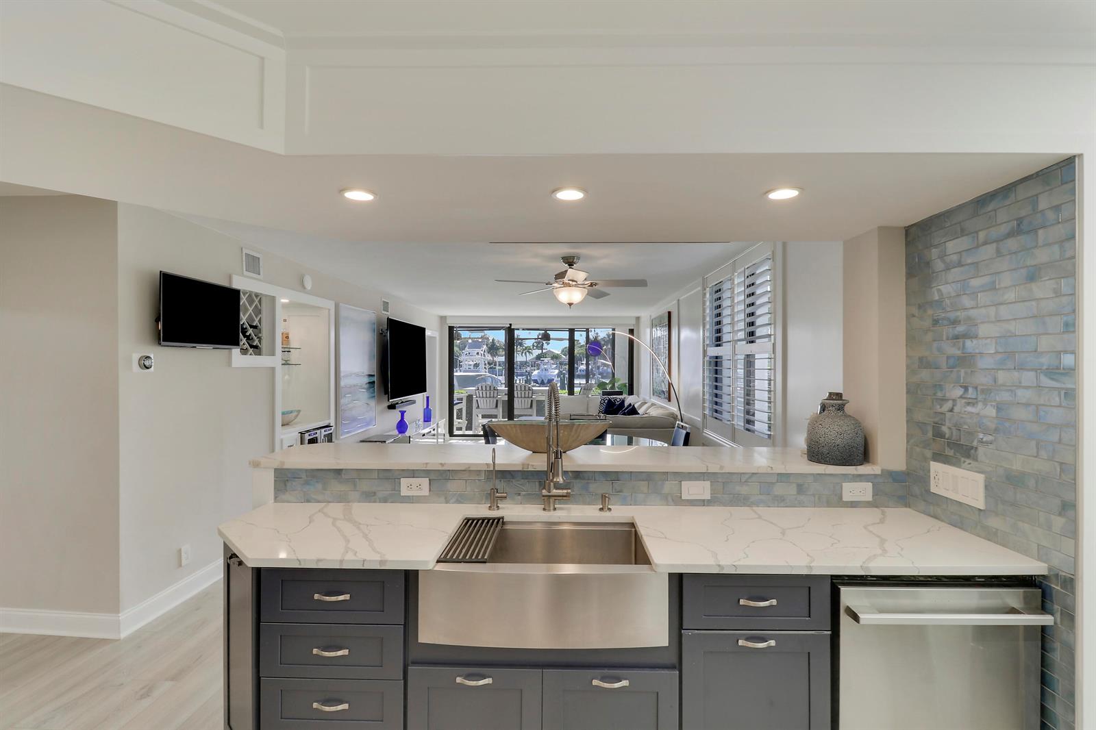 A kitchen with dark blue cabinets, a farmhouse sink, and a marble countertop faces a living area — 515 Bay Colony Drive N, Juno Beach FL 33408, JUNO BEACH, FL