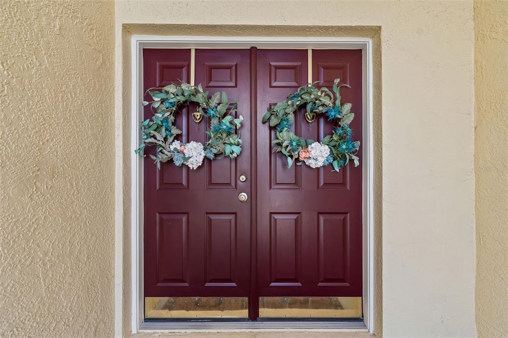 A pair of dark red double front doors with wreaths, set in a beige stucco wall — 10111 KINGSHYRE WAY, TAMPA, FL