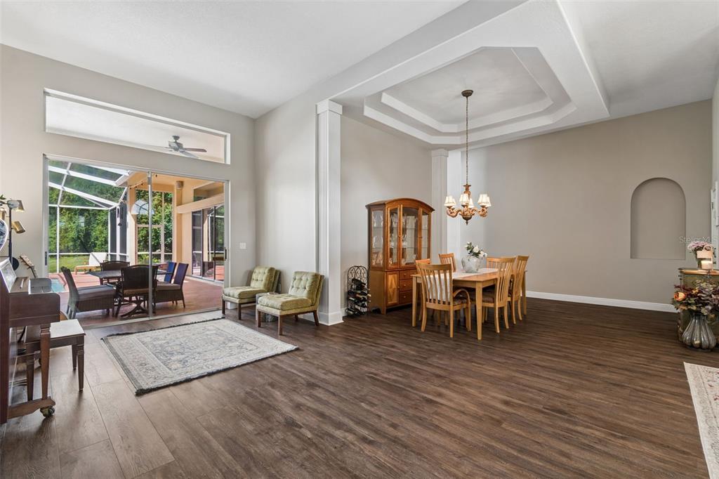 A dining area and living space with wood-look flooring, a tray ceiling, and sliding doors — 10111 KINGSHYRE WAY, TAMPA, FL