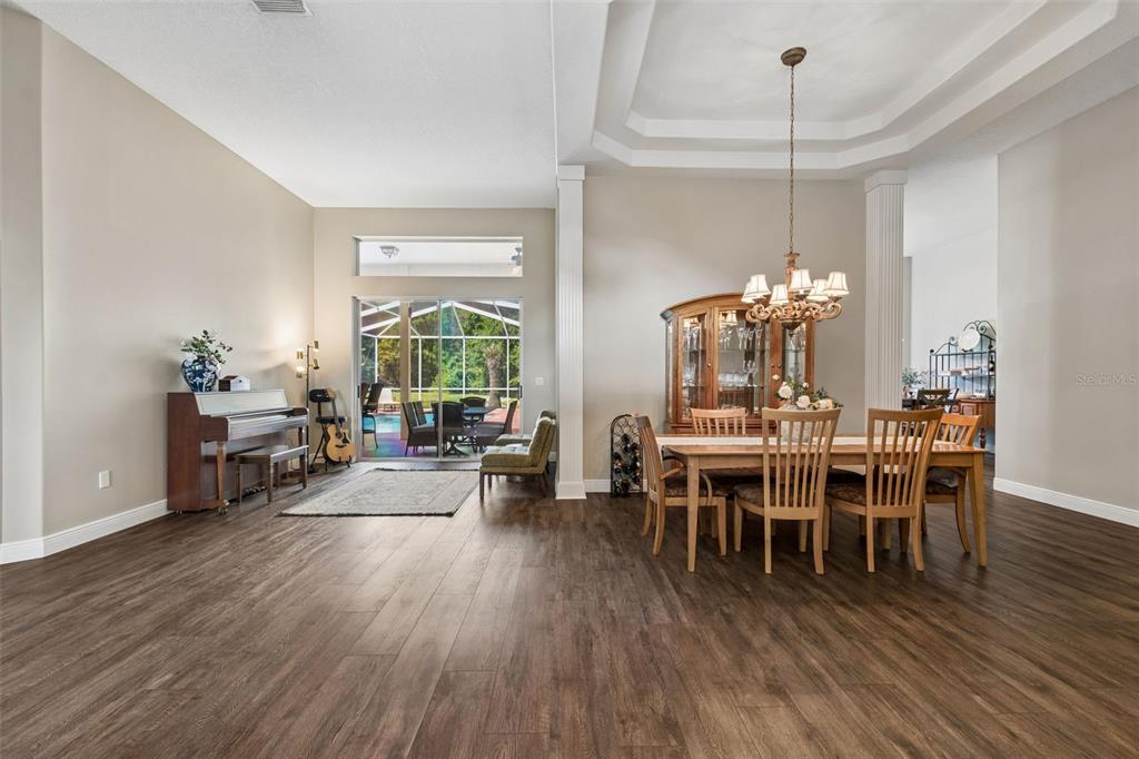 A dining room and living area with wood floors, a piano, and sliding glass doors — 10111 KINGSHYRE WAY, TAMPA, FL