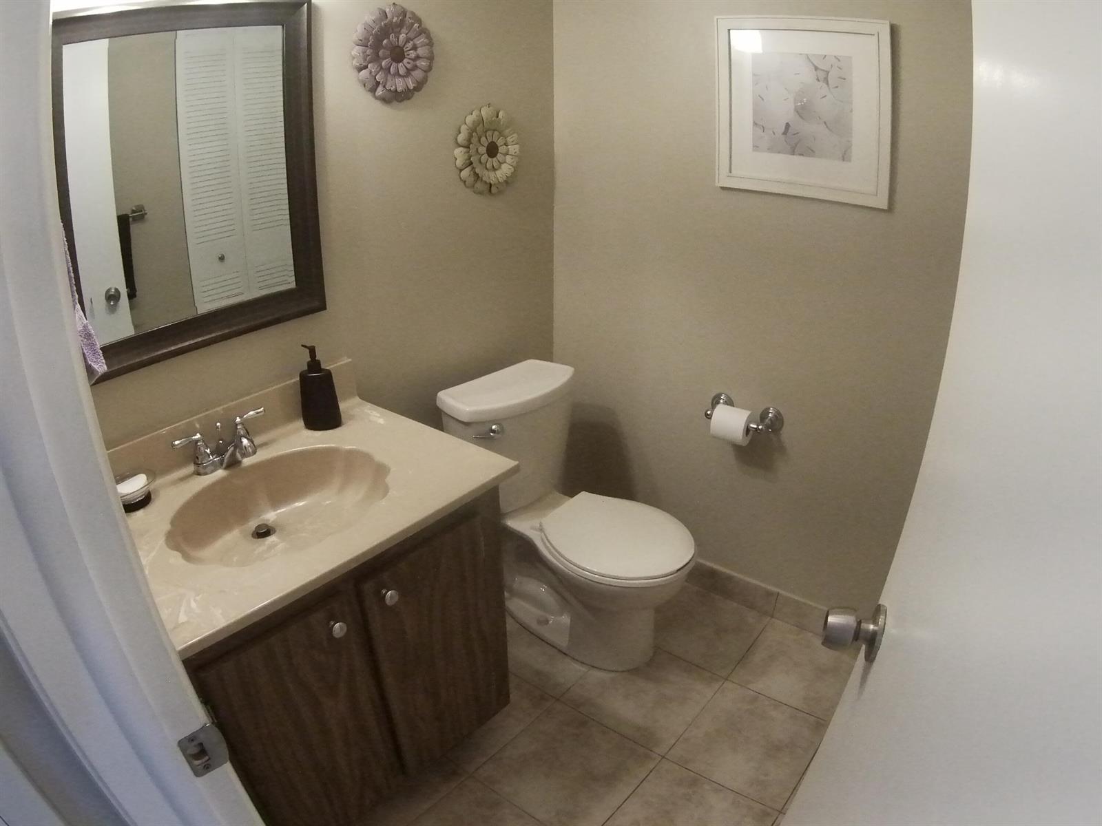 A bathroom features a vanity with a beige countertop, a toilet, and wall-mounted floral decor — 22 CAPRI A, Delray Beach FL 33484, DELRAY BEACH, FL