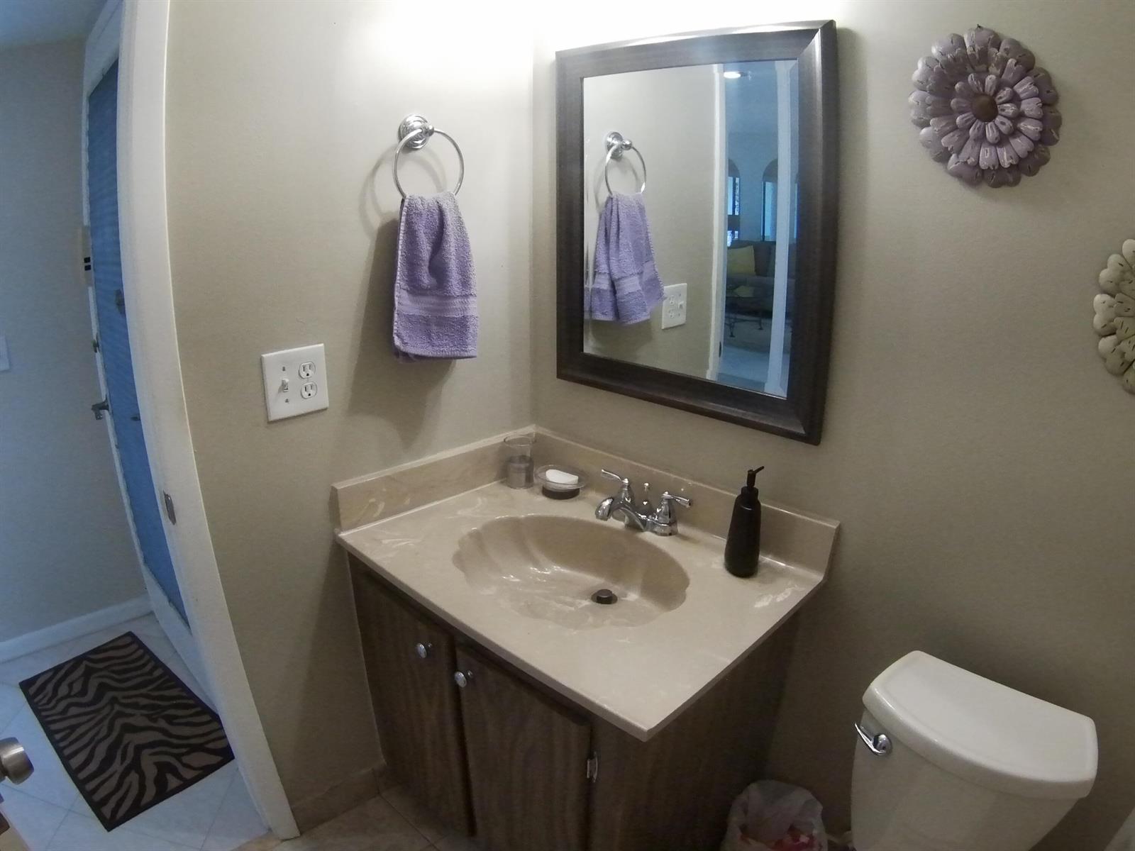 A bathroom features a vanity with a beige countertop, a mirror, and a purple towel — 22 CAPRI A, Delray Beach FL 33484, DELRAY BEACH, FL