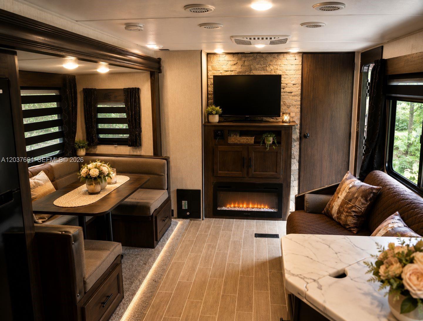 The interior of a recreational vehicle features a dining booth, sofa, fireplace, and television — 735 NE 162nd St # B, Miami FL 33162, MIAMI, FL
