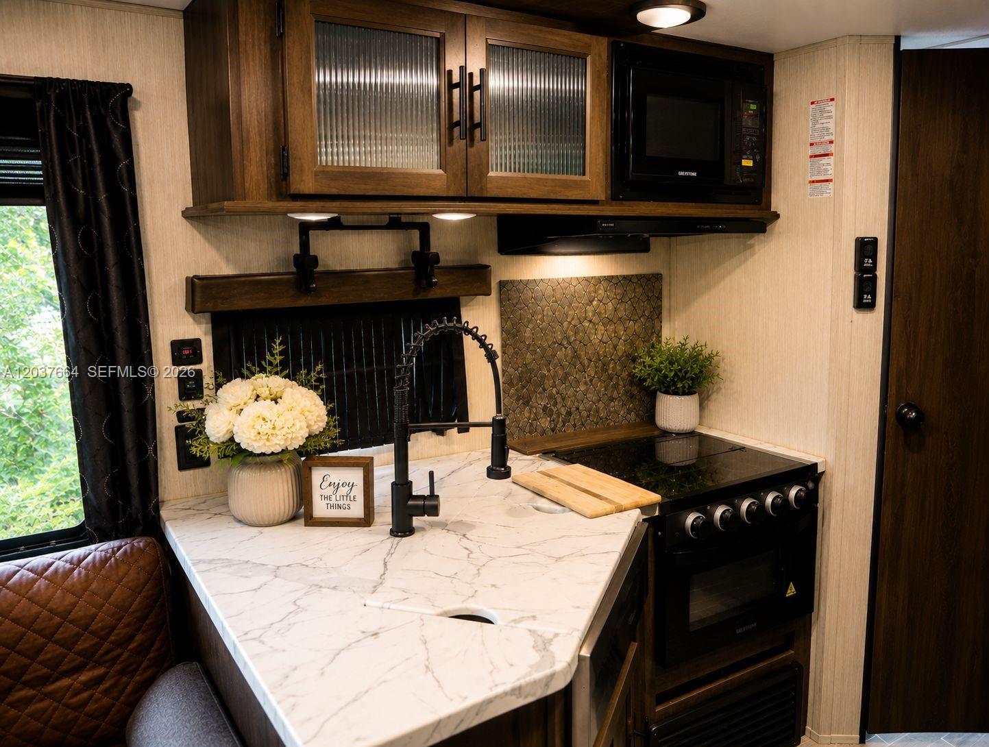 A kitchen in a recreational vehicle features marble-look countertops, dark wood cabinetry, and a stove — 735 NE 162nd St # B, Miami FL 33162, MIAMI, FL