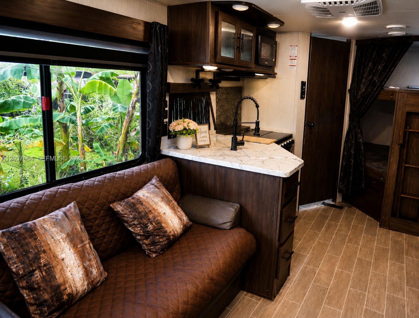 A travel trailer interior features a brown quilted sofa, marble-look countertop, and a kitchen area — 735 NE 162nd St # B, Miami FL 33162, MIAMI, FL