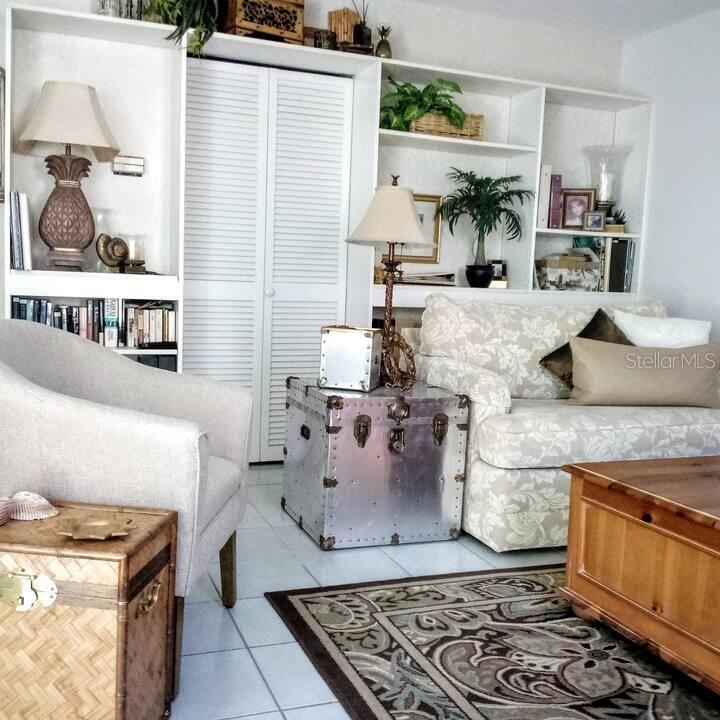 A living room features built-in shelving, a patterned sofa, and a metallic trunk side table — 722 S BLVD OF THE PRESIDENTS UNIT 201, SARASOTA, FL