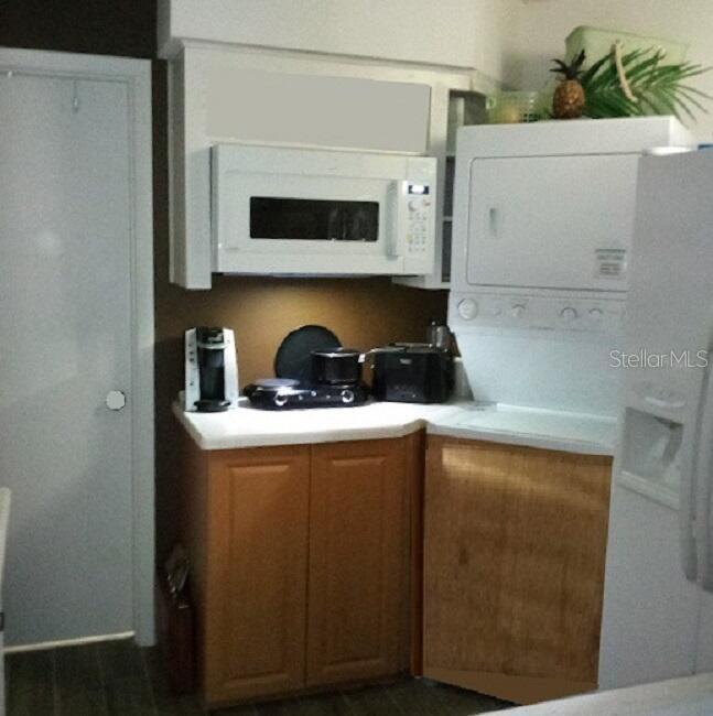 A kitchen area features wooden cabinets, a white microwave, and a stacked washer and dryer — 722 S BLVD OF THE PRESIDENTS UNIT 201, SARASOTA, FL