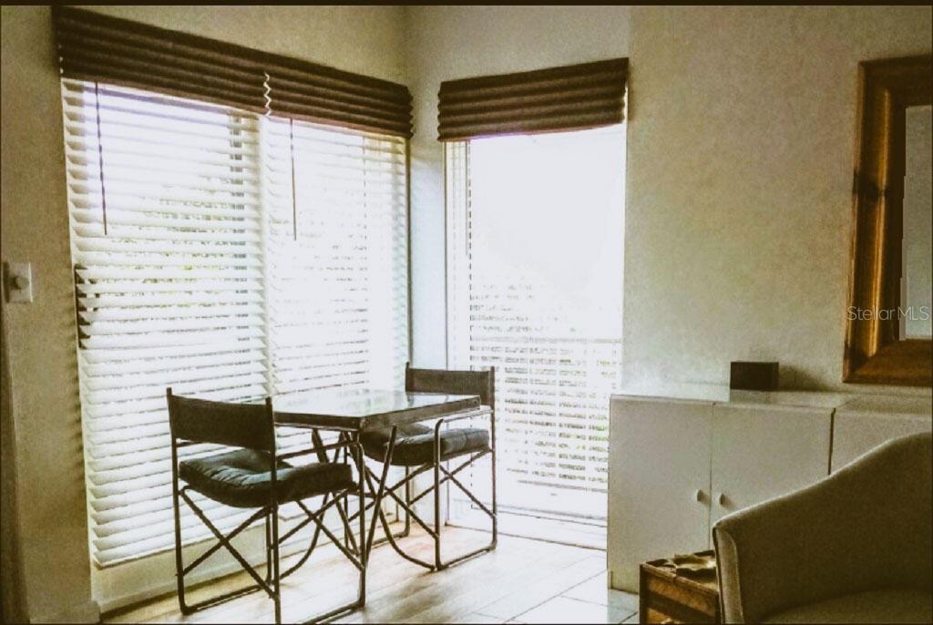 A dining area features a small glass table, two folding chairs, and large corner windows — 722 S BLVD OF THE PRESIDENTS UNIT 201, SARASOTA, FL