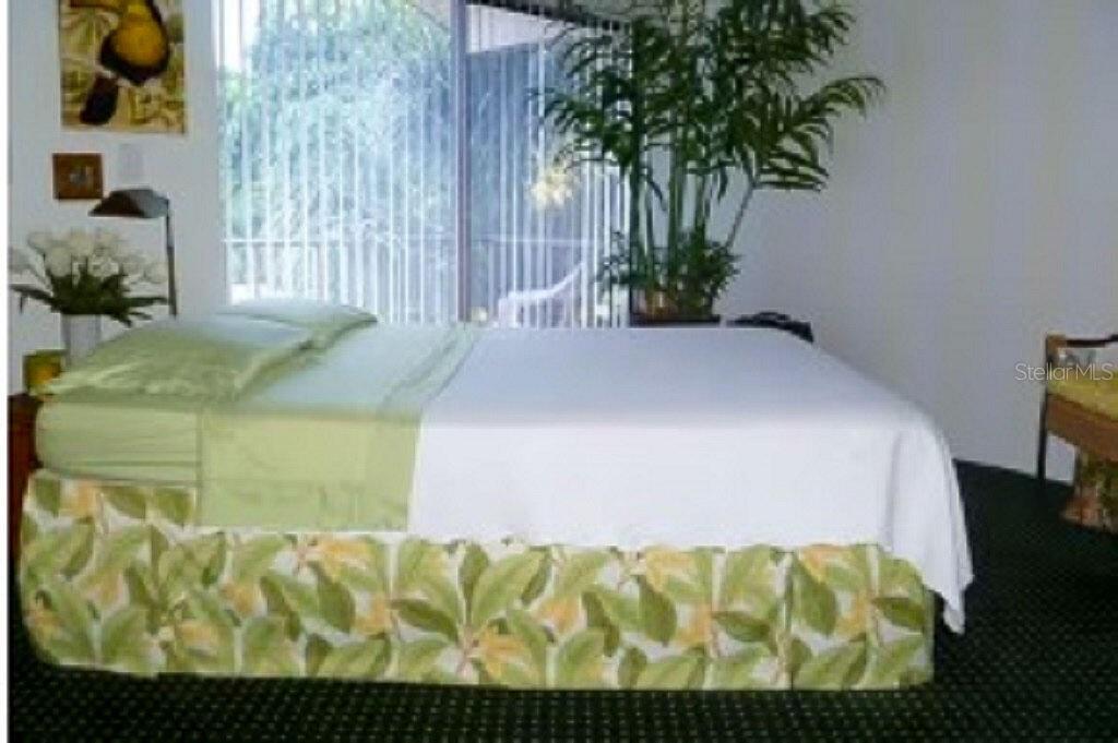 A bedroom features a bed with a tropical-print bed skirt, a large plant, and blinds — 722 S BLVD OF THE PRESIDENTS UNIT 201, SARASOTA, FL